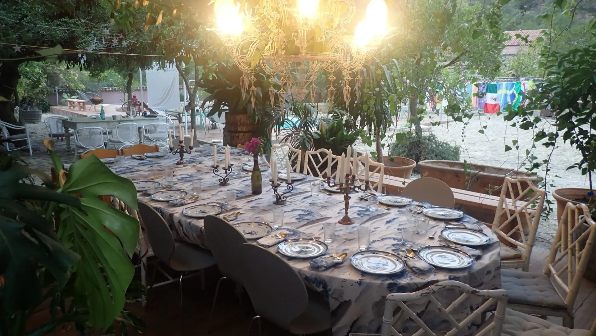 Long table laid under a lit chandelier in the courtyard at dusk.